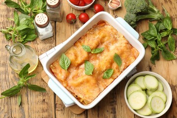 Tasty vegetarian lasagna in baking dish and ingredients on wooden table, flat lay