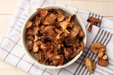 Dried chanterelle mushrooms in bowl on light wooden table, top view