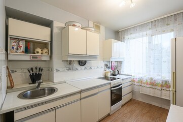 functional kitchen with beige cabinets, a stainless steel sink, and an electric stove. A patterned...