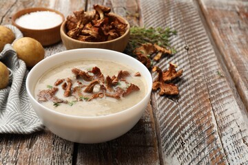 Tasty cream soup with mushrooms and thyme in bowl on color wooden table, closeup
