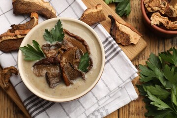 Tasty cream soup with mushrooms and parsley in bowl on wooden table, flat lay