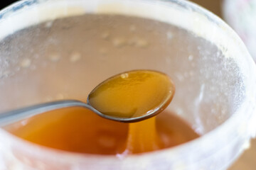 Close-up of golden honey dripping from a spoon into a transparent container, highlighting its smooth texture and natural shine.