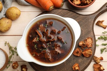 Tasty soup with mushrooms in bowl and products on light wooden table, flat lay