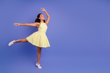 Elegant young woman dancing joyfully in a bright yellow dress on a violet background, celebrating...