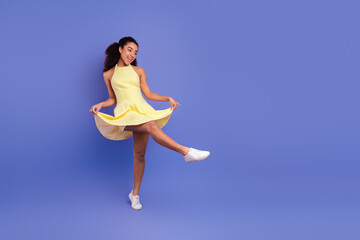 Fototapeta premium Cheerful young woman in a yellow dress posing playfully against a purple background, expressing happiness and vibrant style.