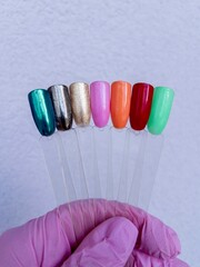Colorful nail polish samples on plastic tips in hand with pink glove