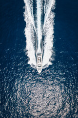 Aerial top down view of a luxury yacht cruising with speed over sparkling ocean and leaving a trail of bubbles and waves behind