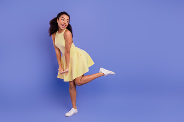 Chic cheerful woman in a yellow dress posing playfully against a vibrant purple background, exuding...