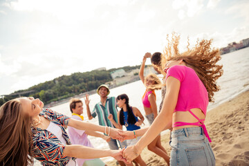 Group of cheerful young friends dancing together during a fun summer outing on a sandy beach with scenic surroundings