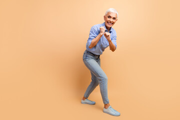 Fototapeta premium Expressive mature businesswoman wearing casual blue striped shirt on beige background showing enthusiastic gesture.