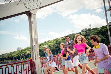 Group of diverse young friends enjoying a lively summer day outdoors on a bridge celebrating good...