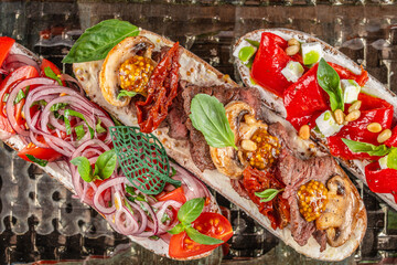 Three gourmet open-faced sandwiches are beautifully arranged, each topped with fresh vegetables, herbs, cheeses, and grilled meats for a visually striking and appetizing presentation