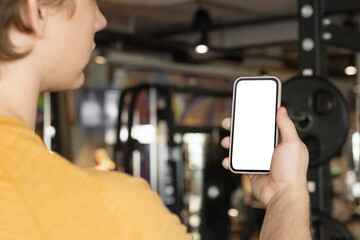 Athlete standing and displaying mobile phone with white blank screen in gym setting. Mock up. Space for design.