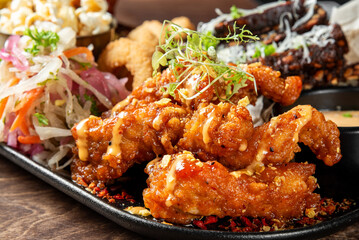 Crispy fried chicken wings with sauce and herbs served alongside a fresh vegetable salad and side dishes on a plate. Close-up of a delicious homemade meal.