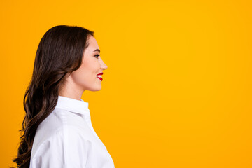 Side profile of a stylish brunette woman in a white shirt set against a vibrant yellow background,...