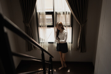 Sad and depressed young asian woman standing at window in the bedroom, Woman worry, Unhappy girl.