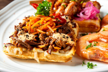 Gourmet waffles with shredded meat, creamy sauce, shrimp, pickled onions, and herbs, artfully plated for upscale dining or culinary presentation.