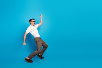 Obraz premium Young stylish man posing joyfully against a blue background, expressing casual elegance and vibrant energy