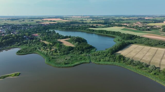 Aerial view of a serene lake surrounded by lush greenery and agricultural fields, creating a mosaic of colors and textures, Brussow, Brandenburg, Germany.