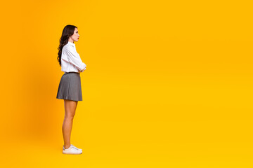 Side profile of a young fashionable woman in a white shirt and grey skirt against a bright yellow background