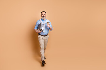 Fototapeta premium Confident senior businessman with books and coffee enjoys elegant casual style against a beige background