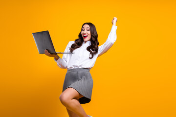 Excited businesswoman holding a laptop on a yellow background expressing success and enthusiasm...