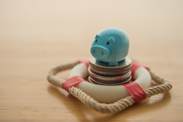 Blue piggy bank and stack coins in lifebuoy on wooden table background. Savings protection, financial risk management and security, savings insurance, personal and home finance and so on concept.