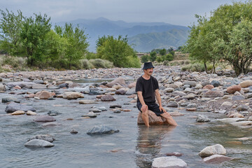 Senior Man Sitting on Rock in Mountain River, Kazakhstan