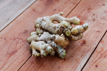closeup of raw fresh ginger root placed on rustic brown wooden table surface.