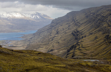 Fototapeta premium coastal landscape with terraced mountain slope and snow covered mountain peeks, Berufjörður fjord, Öxi pass, East Iceland