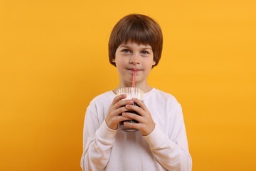 Cute little boy drinking refreshing soda on orange background