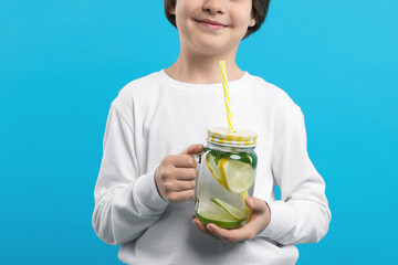 Little boy with mason jar of lemonade on light blue background, closeup. Refreshing drink