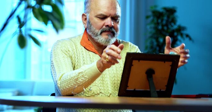 Indian senior man with photo frame showing deep emotions while remembering loved ones, hugging framed picture with nostalgia, emotional elderly person grieving quietly at home in solitude