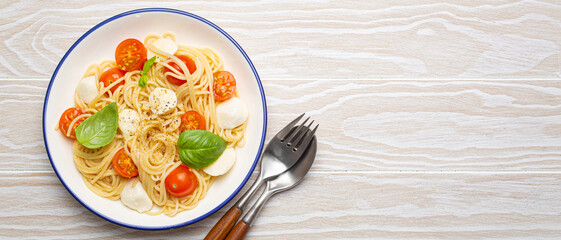 Top view of a plate of spaghetti pasta with cherry tomatoes and mozzarella cheese on a white wooden background with copy space