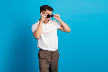 Stylish young man wearing sunglasses makes surprised gesture against a blue background, embodying...