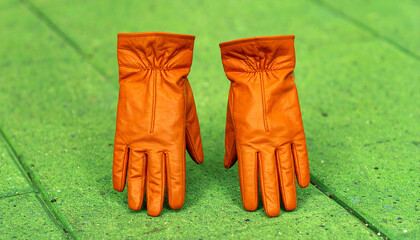 Pair of orange leather gloves standing upright on bright green textured floor. Vibrant color contrast and symmetry.
