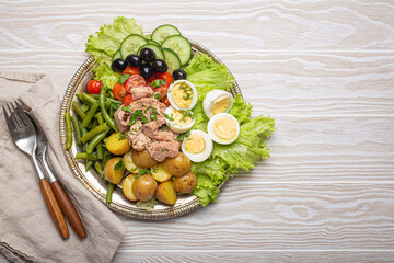 Delicious nicoise salad with tuna, eggs, potatoes, green beans, and olives on white wooden table...