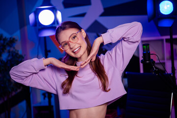 Young female blogger with a bright smile in a neon-lit studio showcasing modern social media...