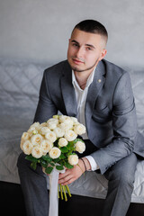 Groom in formal attire holding bouquet of white roses in an elegant indoor setting