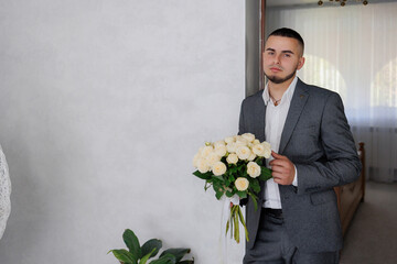 Groom holding white roses in a bright indoor setting before the wedding ceremony
