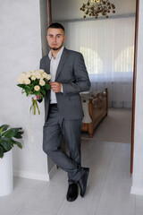 Man in formal suit holds bouquet of white roses in modern home setting