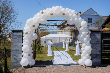 Beautiful wedding arch decorated with balloons leads to outdoor ceremony area in springtime