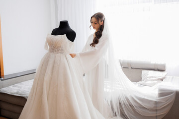 Bride prepares for wedding day while adjusting her elegant gown near soft natural light