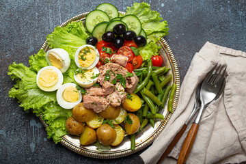 Classic French Nicoise salad with tuna, eggs, potatoes, green beans and olives on a silver platter