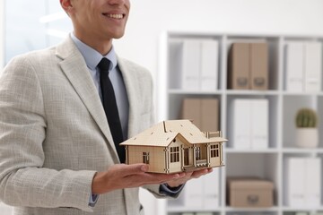 Real estate agent holding house model in office, closeup. Space for text