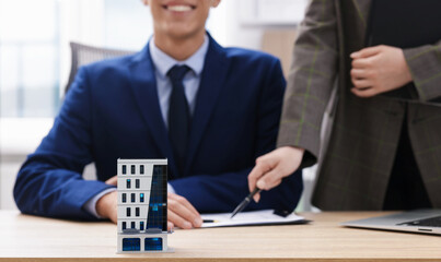 Real estate agent working with client at desk in office, focus on house model