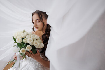 Bride in elegant attire holds bouquet under flowing fabric in soft lighting