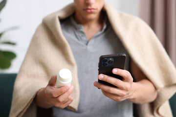 Man with pills having online consultation with doctor via smartphone at home, closeup
