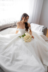 Elegant bride in a stunning white gown holding a bouquet of roses in a modern living room