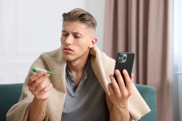 Man with thermometer having online consultation with doctor via smartphone at home